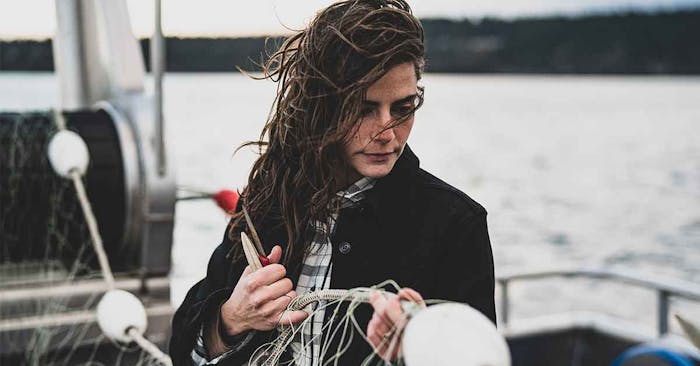 woman in black coat holding a floater on a fishing net while standing on a boat