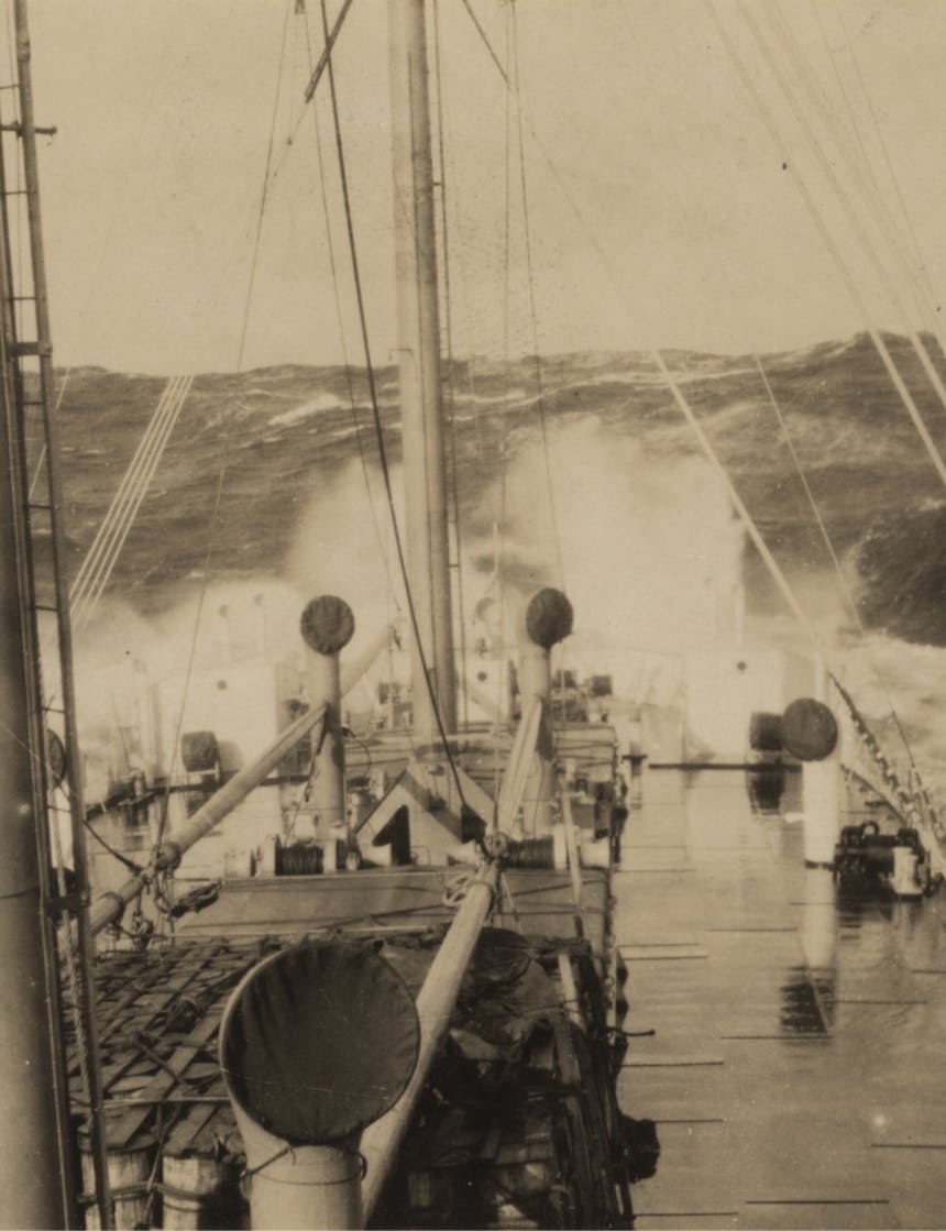 black and white image of the bow of a ship dipping into rough seas sending ocean spray into the sky