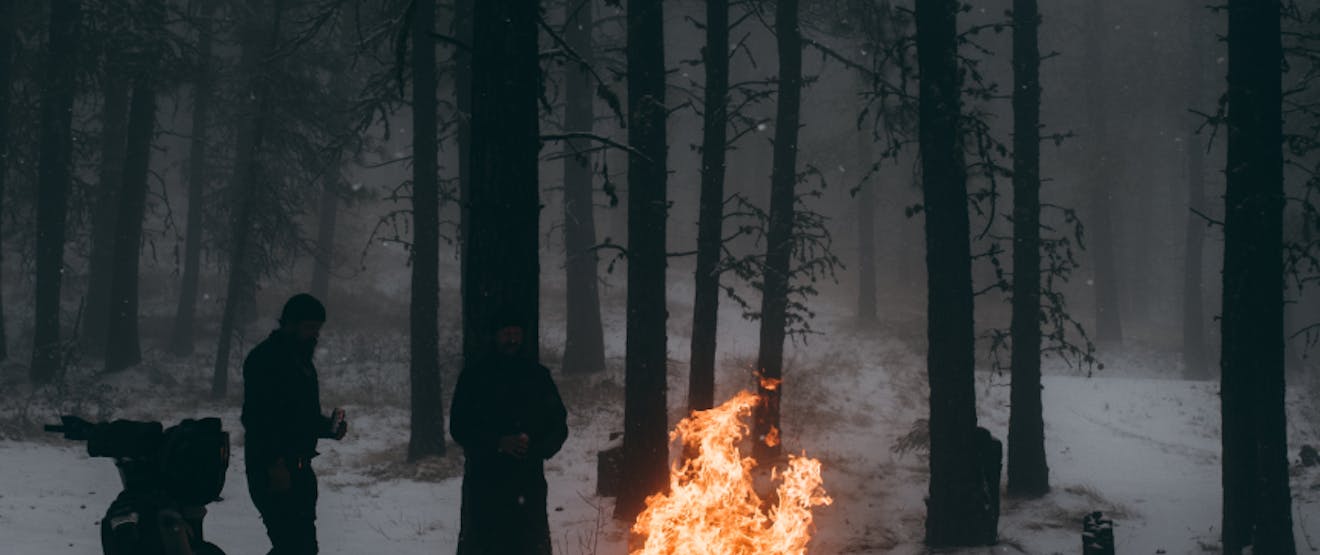 people in a snowy campsite stand next to a very large fire