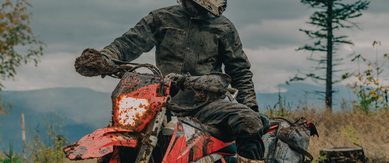 dirt covered orange and white motorcycle and person in black coat and pants covered in mud sitting on motorcycle