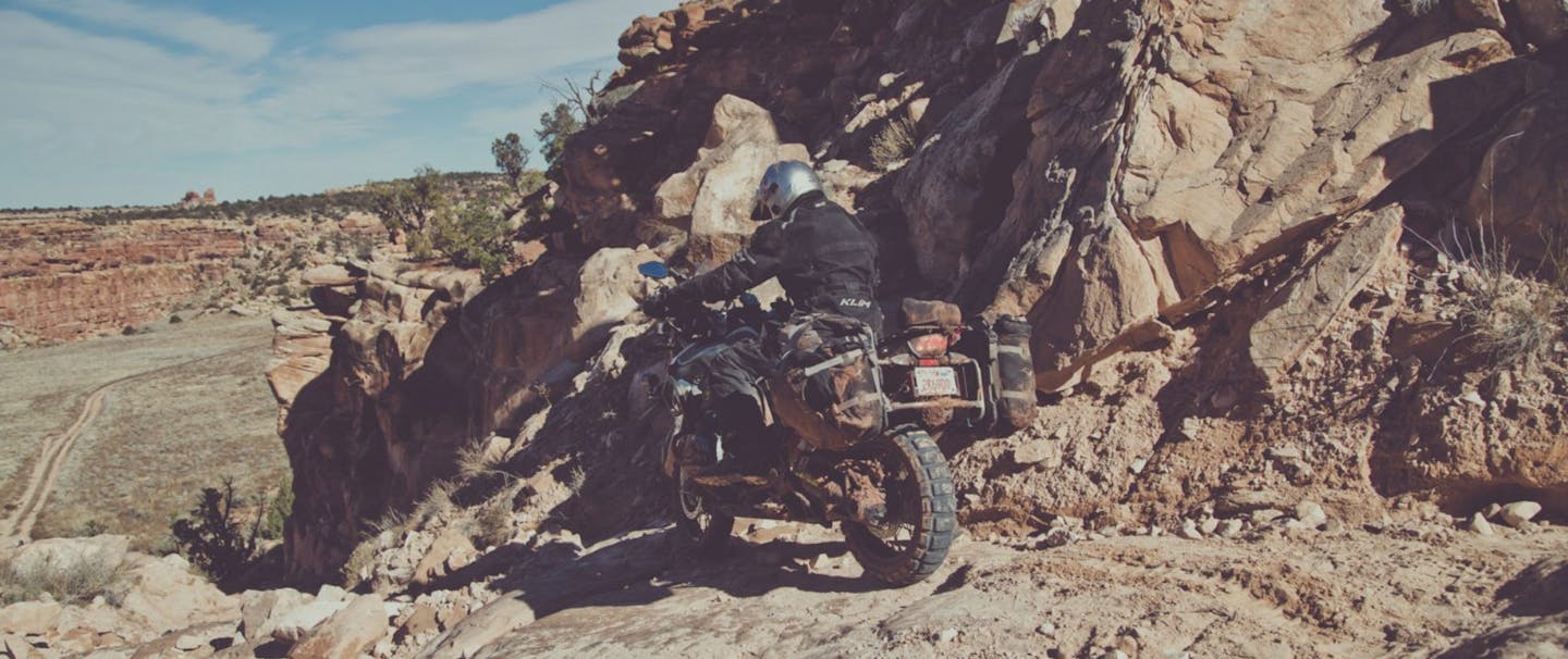 person in silver helmet and black jacket riding a motorcycle down a rocky embankment in the high desert of the Utah Canyonlands