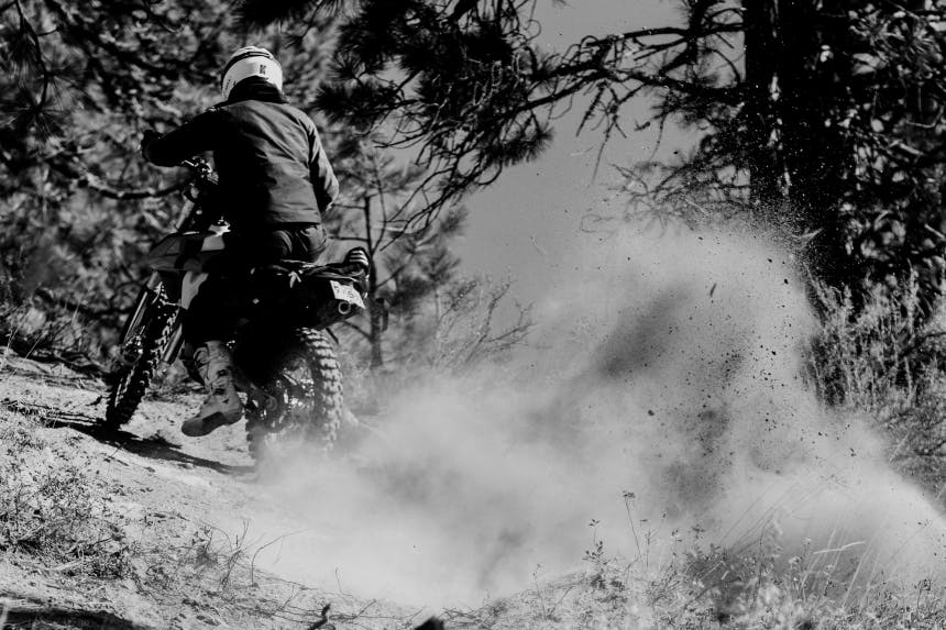 person wearing a white helmet riding a motorcycle kicking up lots of dust