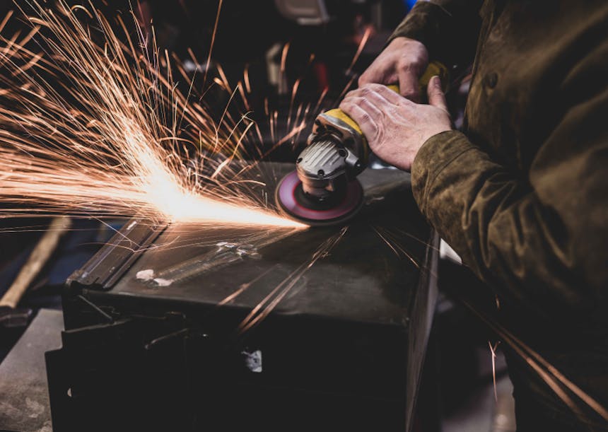 hands using an angle grinder kicking up sparks off the side of an ammo cannister