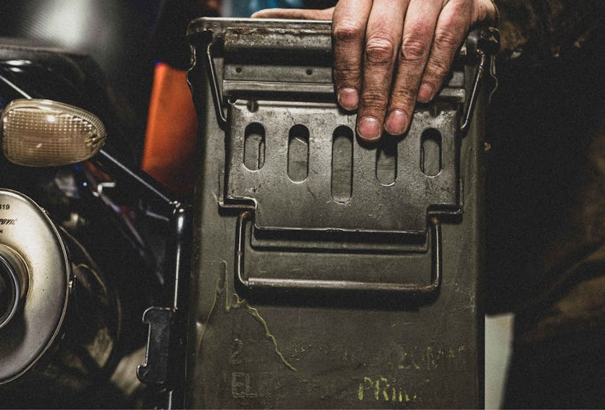 hand on a green mounted ammo cannister on the back of a motorcycle