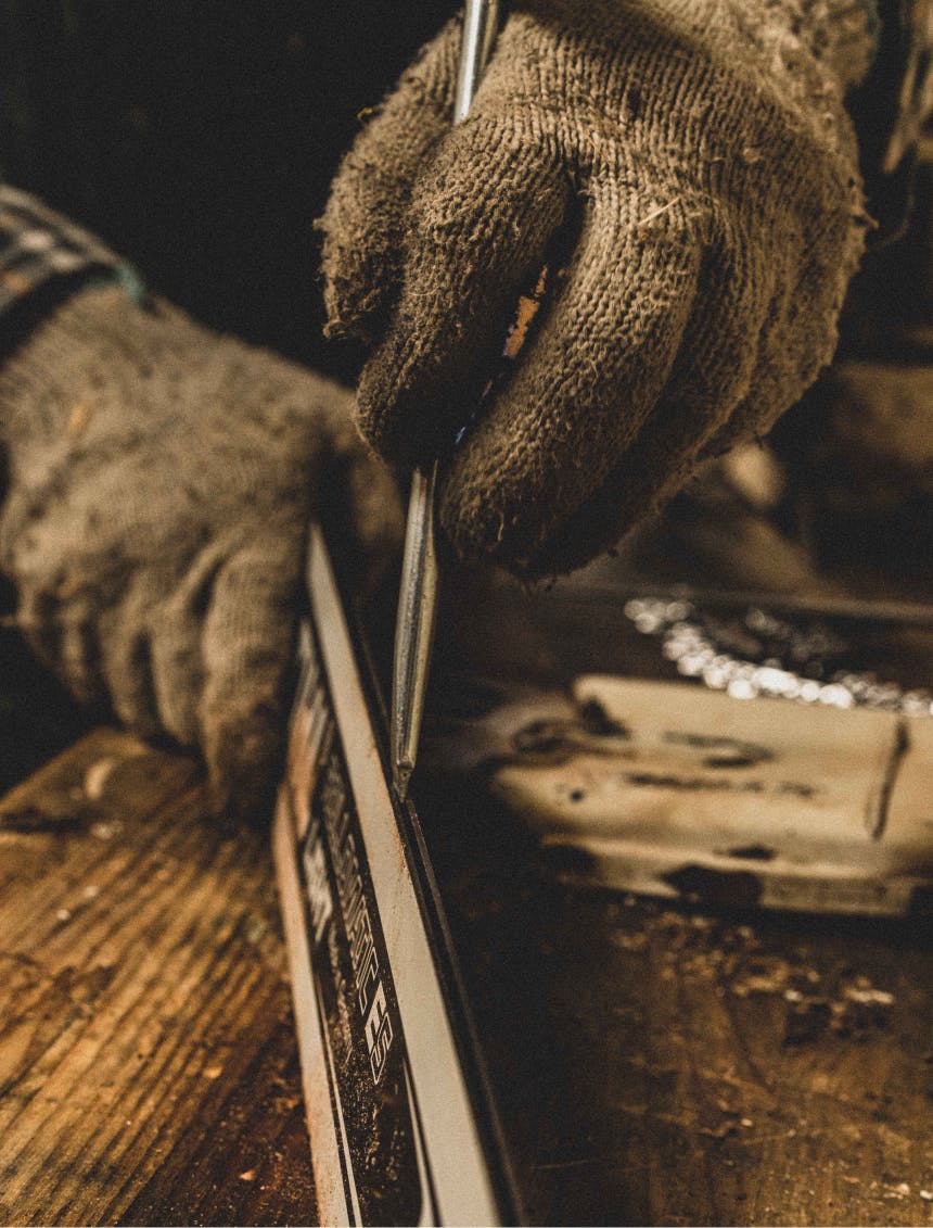 hand using a metal tool to clean out the groove of a chainsaw blade on a wood workbench