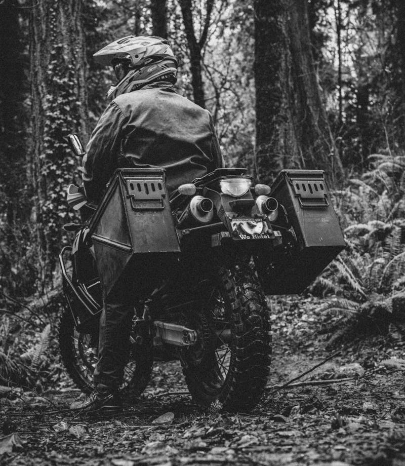 person in helmet and jacket standing motorcycle up in a forest
