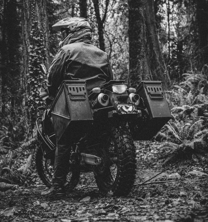person in helmet and jacket standing motorcycle up in a forest