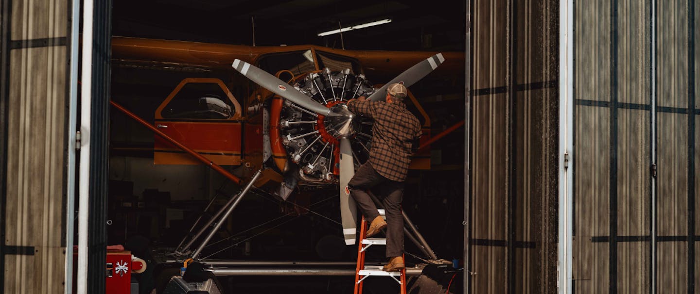 an exterior shot of a man working on the propeller of a float plane in a mechanic plane hanger