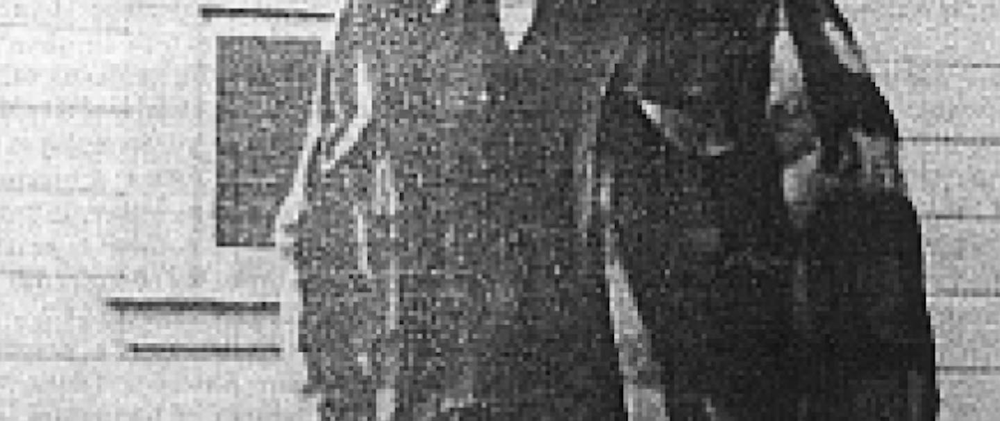 an old black and white pixelated image of a white haired old bearded man, wearing a flannel wool shirt and wool pants standing next to a wood cabin using a cane to hold him up