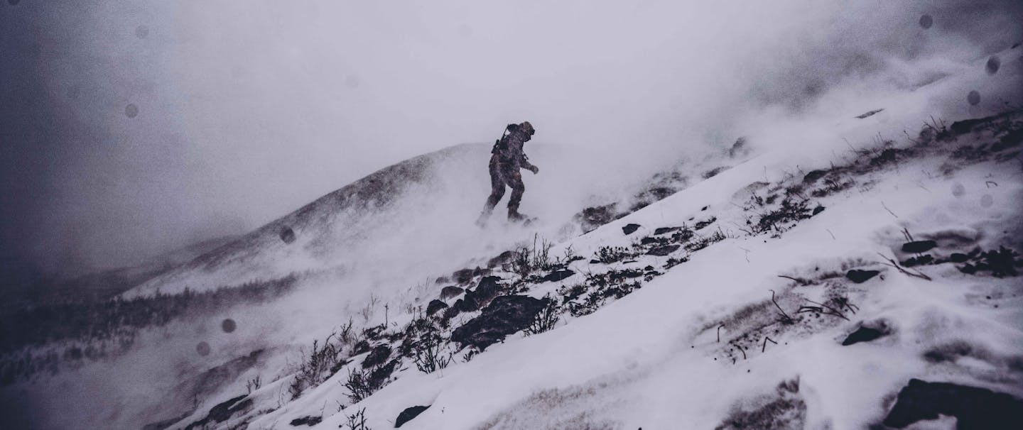 a man wearing several warm layers walking up a rocky and snowy incline