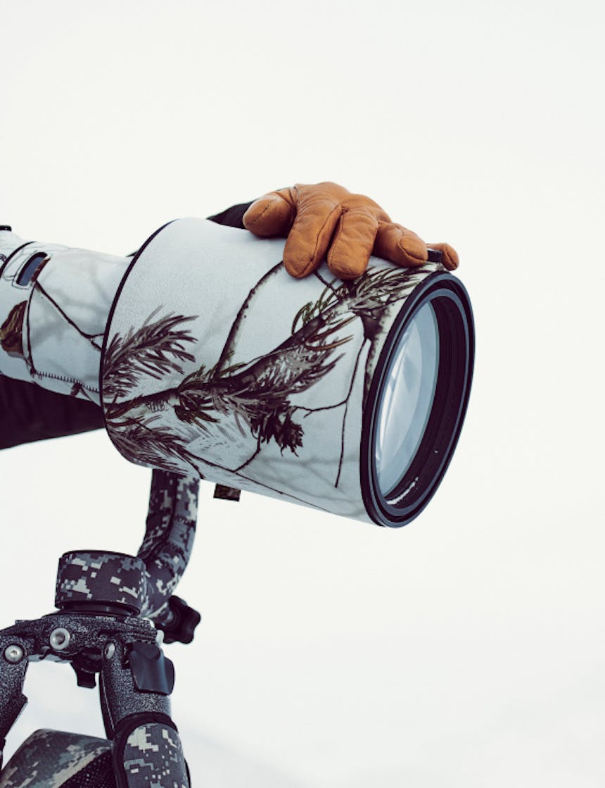 a close up of a huge white camera lens with camouflage on the lens and tripod