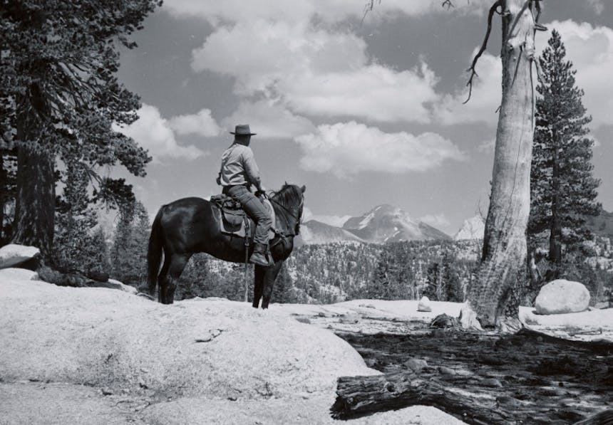 black and white photo of a cowboy in the saddle of a brown horse looking off towards the mountains