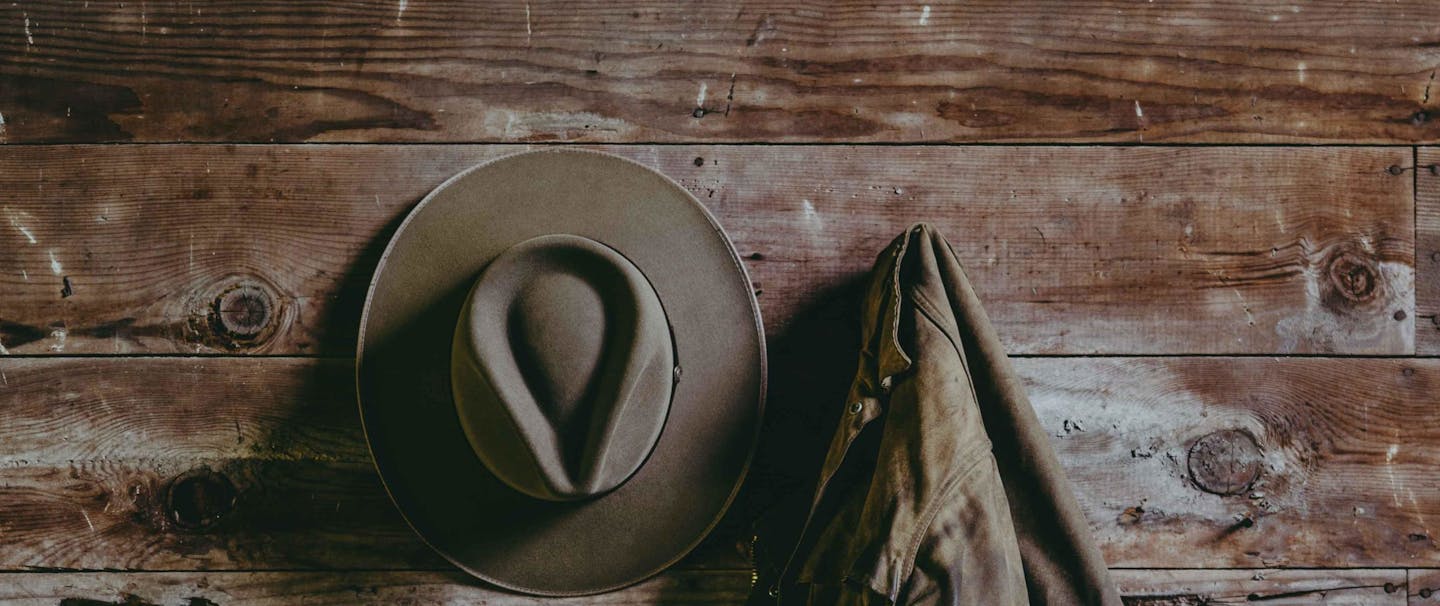 close up of a tan cowboy hat hangin on a tack wall in a barn beside a work jacket