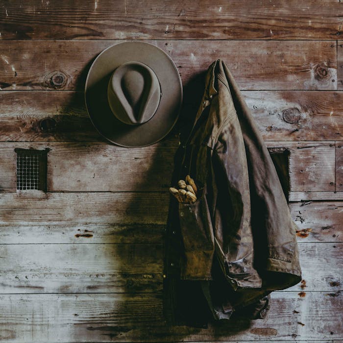 close up of a tan cowboy hat hangin on a tack wall in a barn beside a work jacket