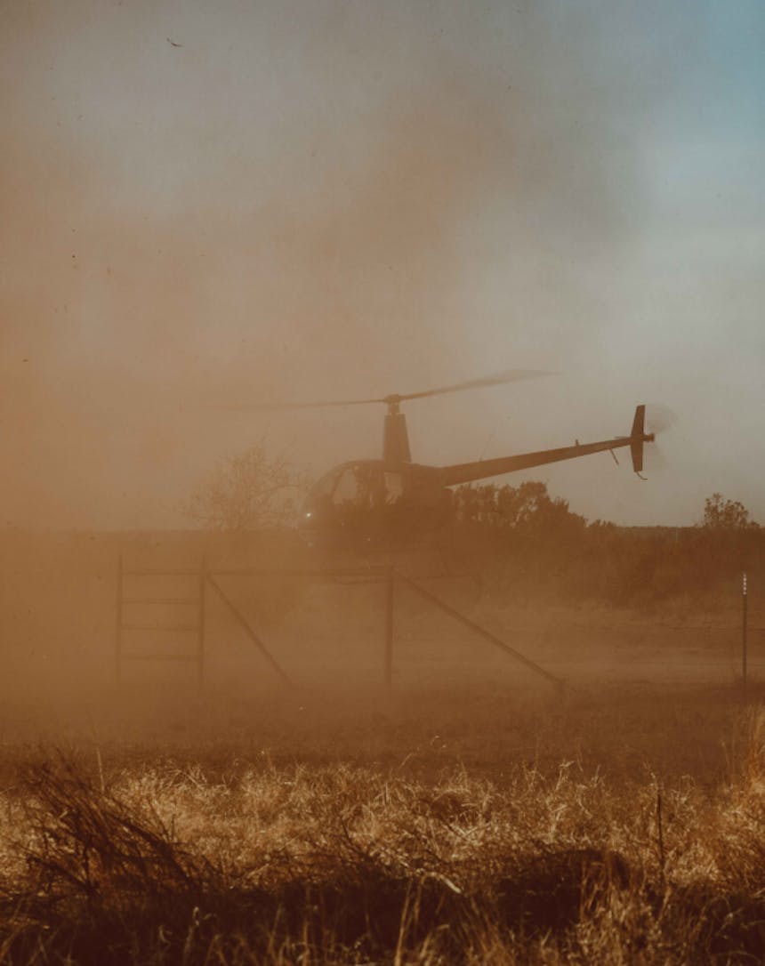 a dusty field as a helicopter takes off