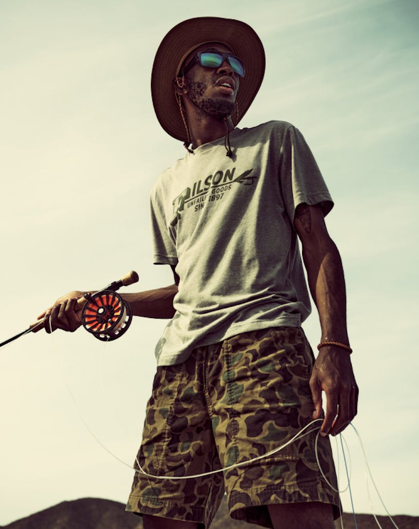 close up of an African American man wearing a grey t-shirt and camo shorts fly fishing