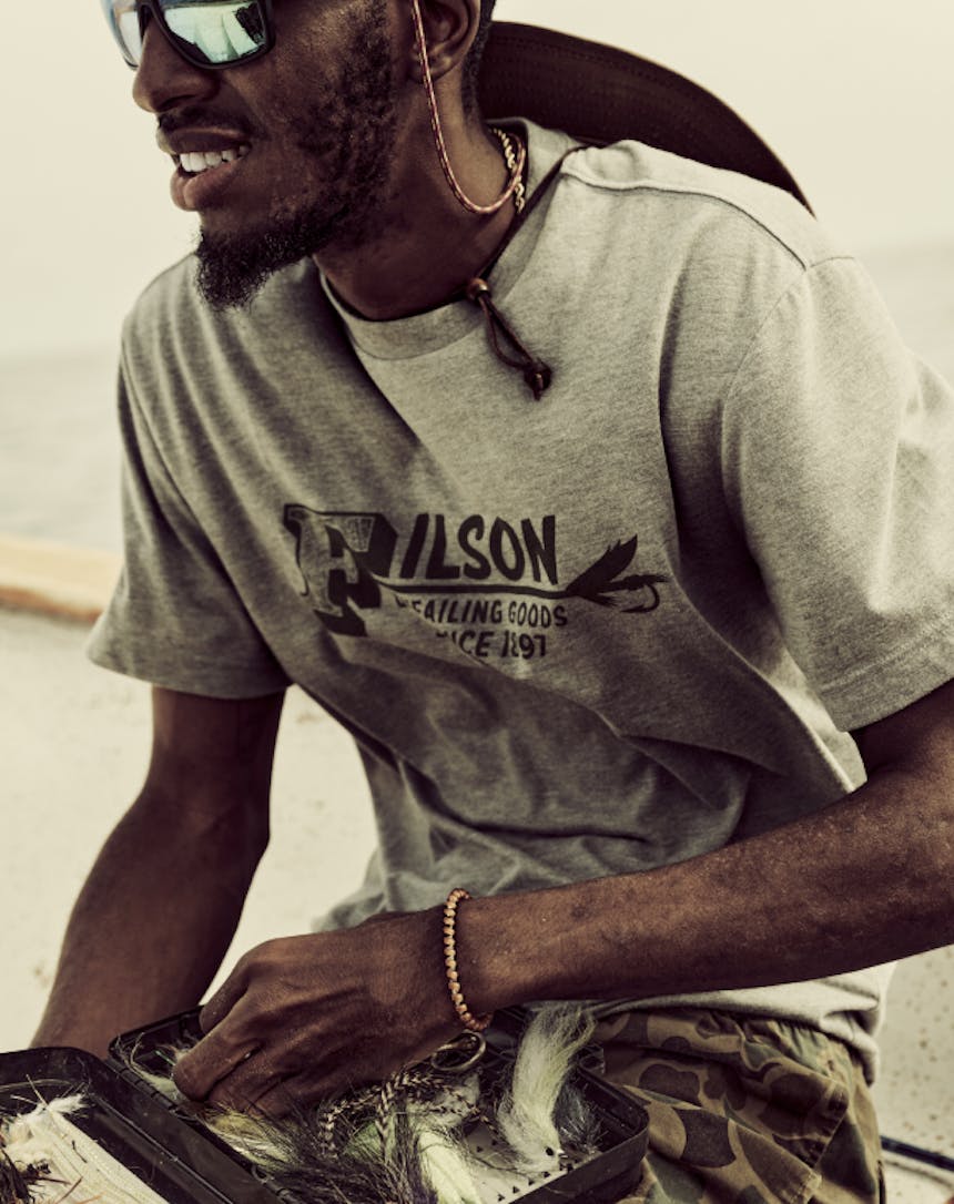 close up of an African American man wearing a grey t-shirt and camo shorts looking through a fly box full of salt water flies for fly fishing