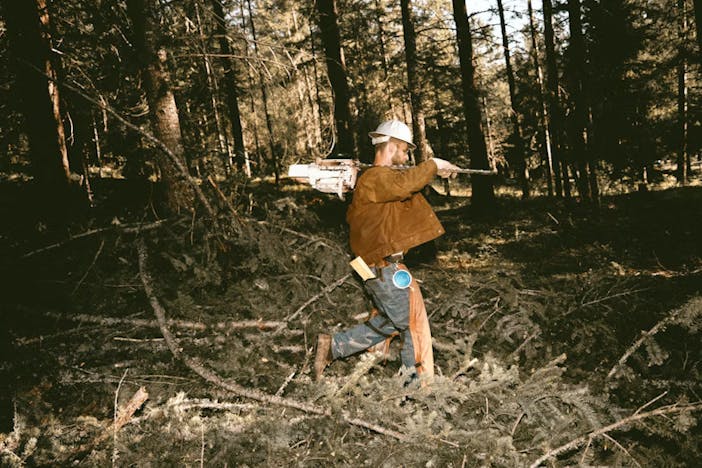 Man works in a forest wearing a Filson Tin Cloth Work Jacket