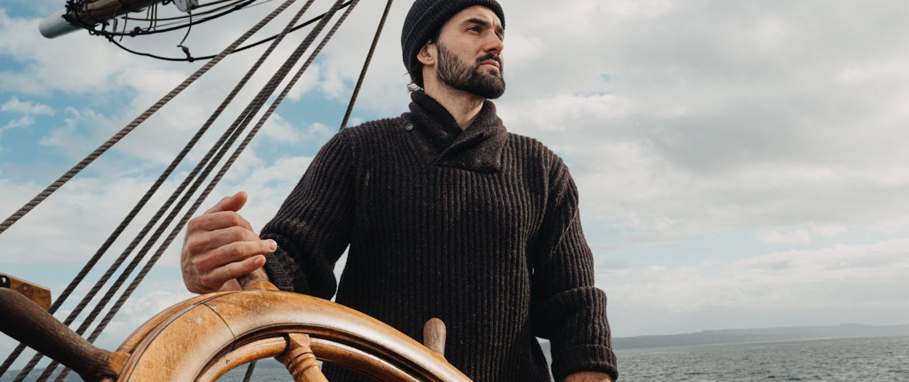 man the helm of the boat wearing a sweater