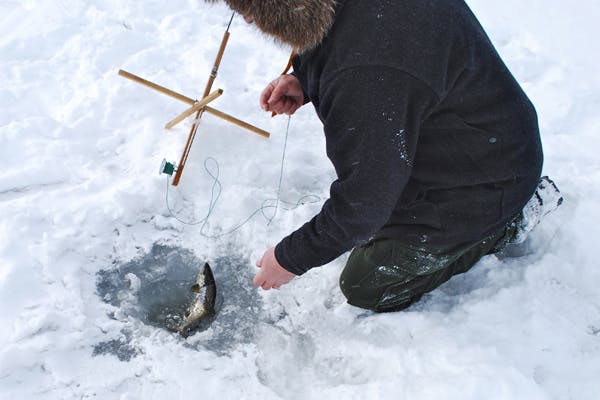 Using a skimmer to remove ice from an ice fishing hole drilled by