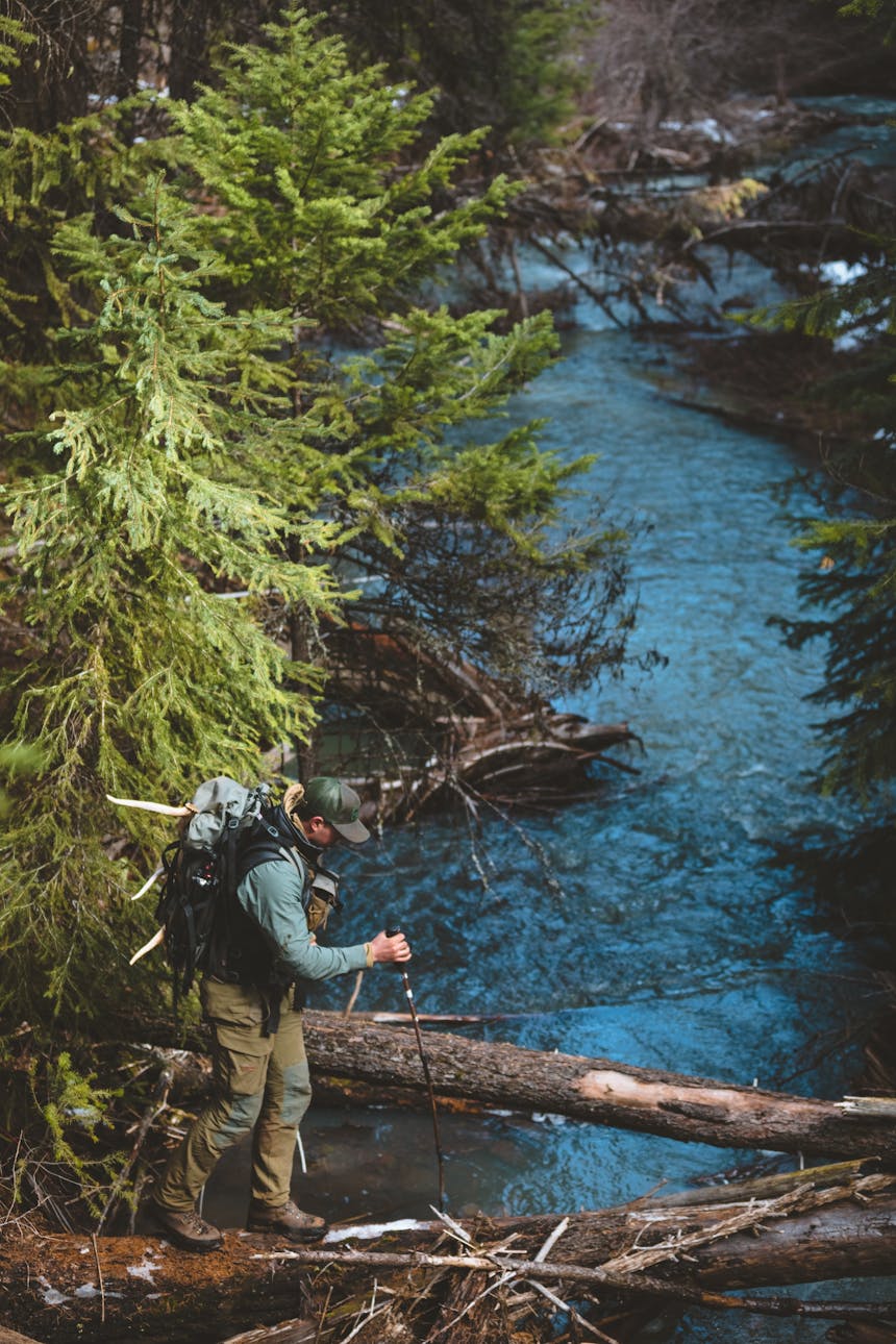 man walking across a log over a creek