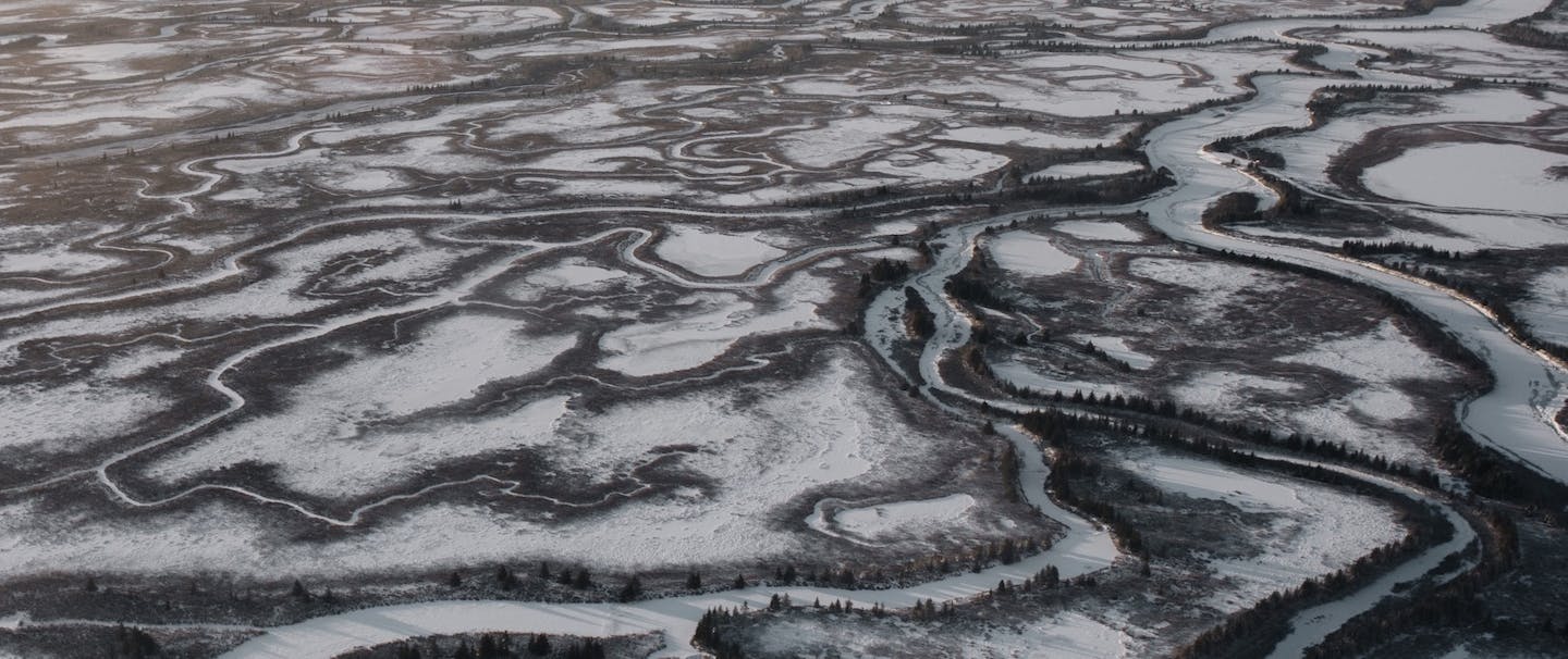 frozen river lists through open expanse of barren snowy land