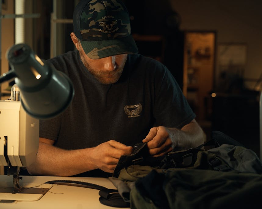 Smokejumper works on gear at sewing machine table
