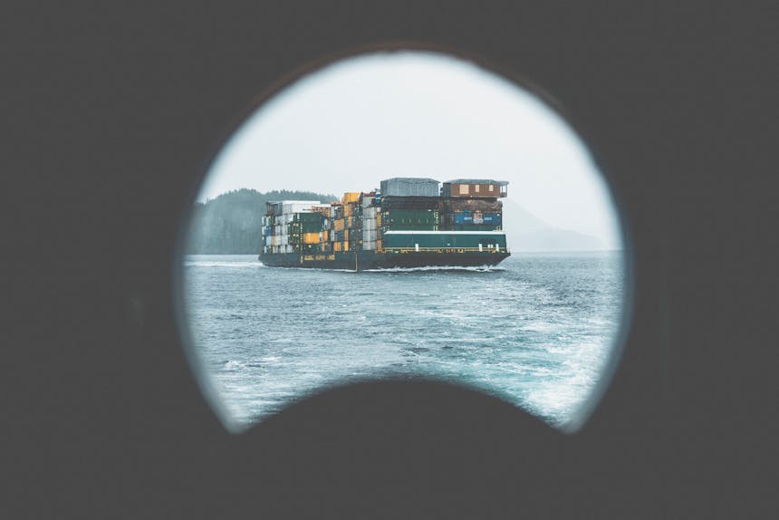 barge with trucking containers seen through porthole of another ship