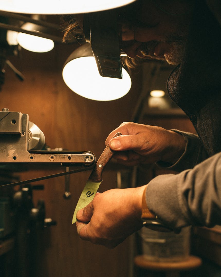 close up of man wearing protective eyewear sharpening knife in a workshop