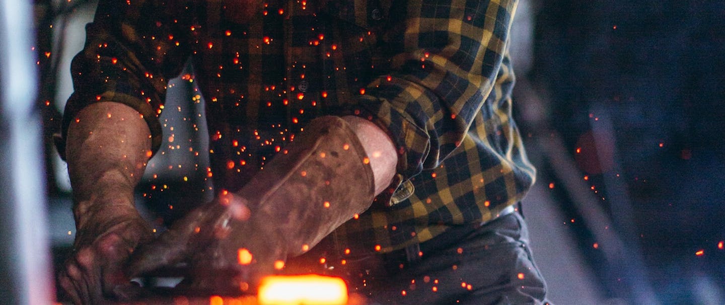 person in brown gloves holding red hot piece of metal at metal shop