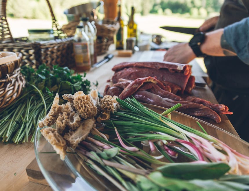 food prep with gathered herbs and mushrooms and meat being cut