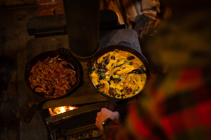 cooking scramble and steak on top of wood fired stove in cast iron skillet